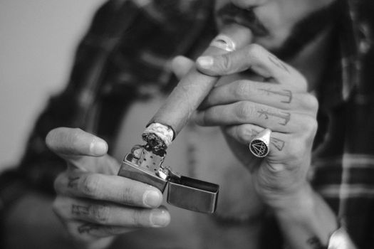 Black and white close-up of a man lighting a cigar with a lighter.