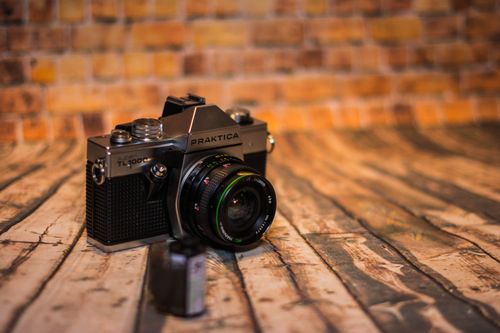 Free Close-up of a vintage Praktica camera on a rustic wooden surface against a brick wall. Stock Photo