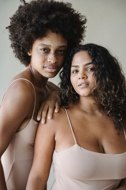 Two confident women with natural curly hair and freckled skin, posing gracefully.