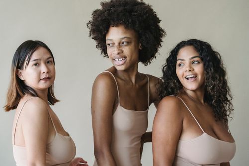 Free Three women of different ethnicities smiling and posing in neutral-toned swimwear. Stock Photo
