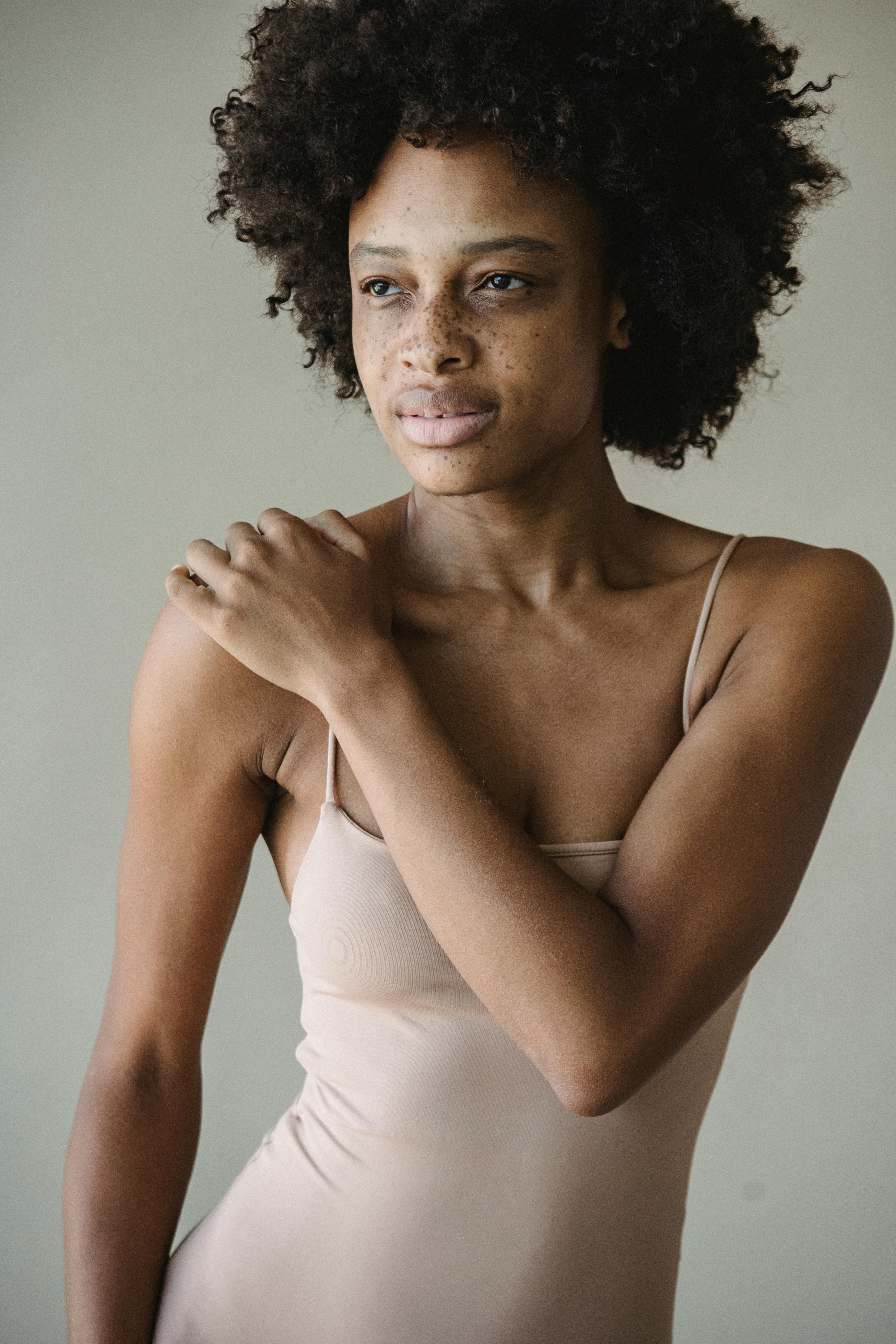 Portrait of a woman with afro hair and freckles posing in a studio setting.