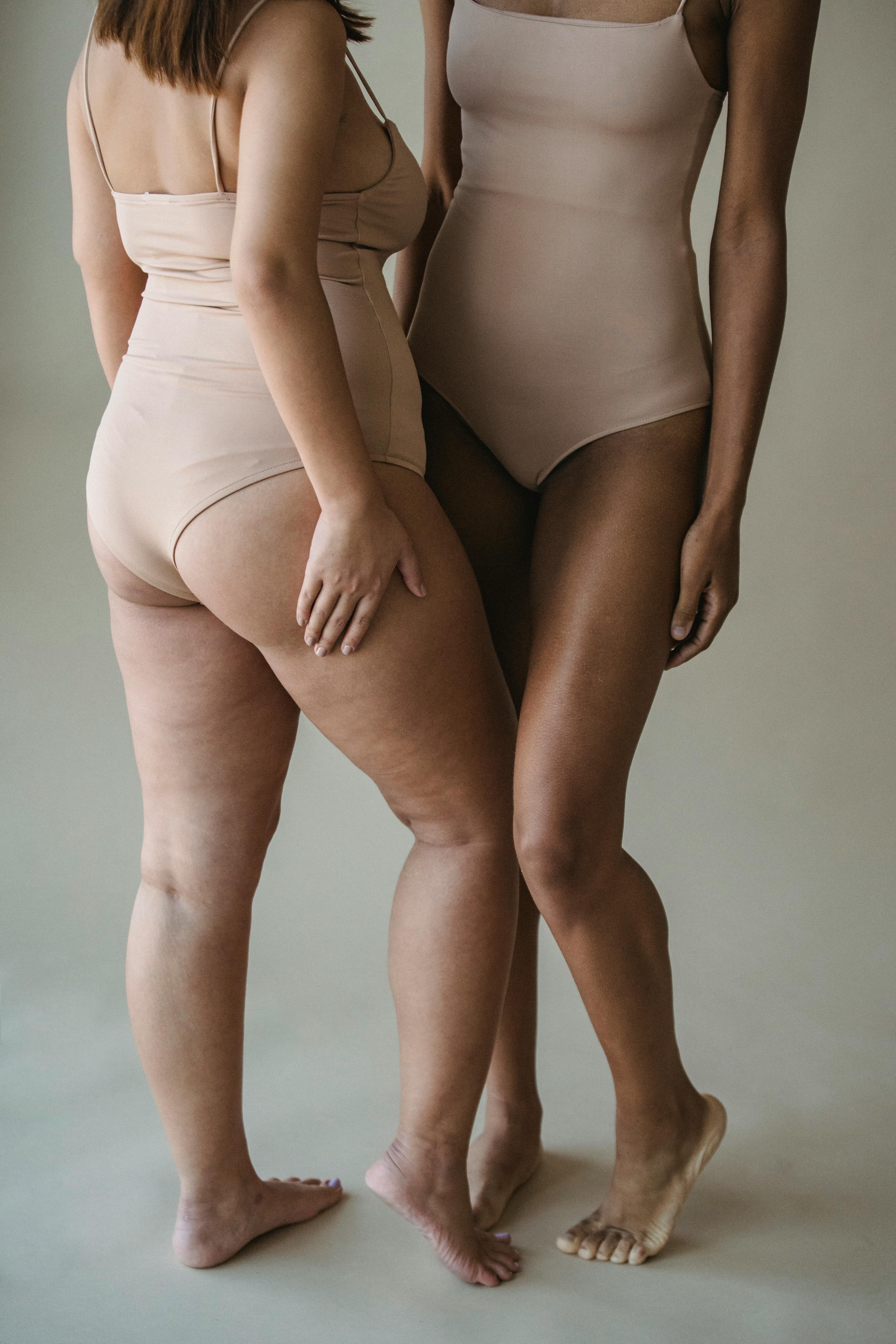 Two women confidently standing in nude bodysuits, embracing body positivity.