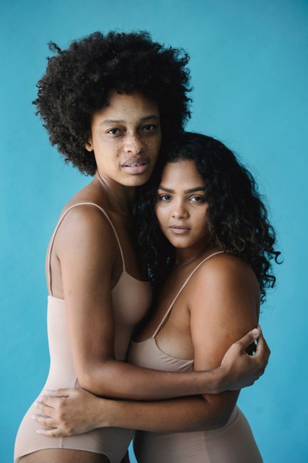 A tender portrait of two women embracing against a blue background, showcasing diversity and connection.