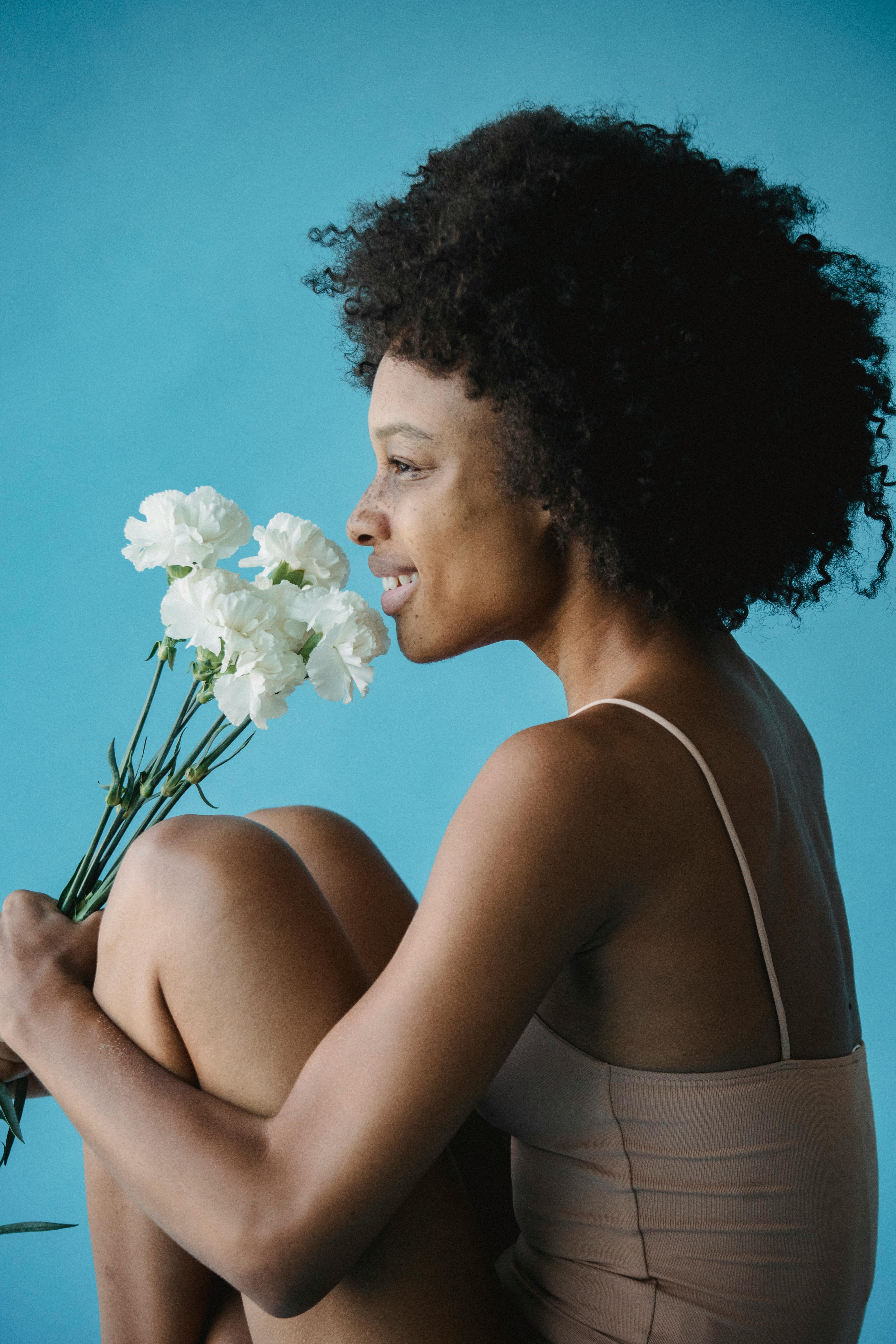 A smiling woman with curly hair holding white flowers against a blue background.