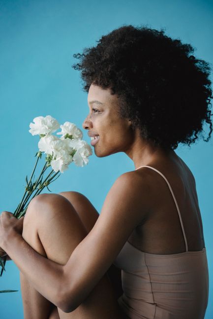A smiling woman with curly hair holding white flowers against a blue background.