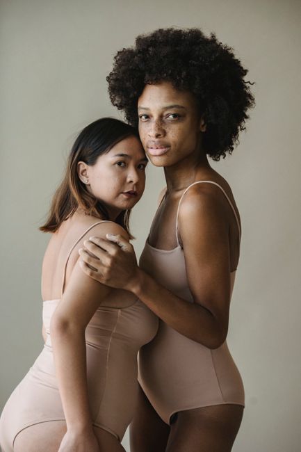 An empowering studio portrait showcasing diversity and natural beauty with two women in bodysuits.