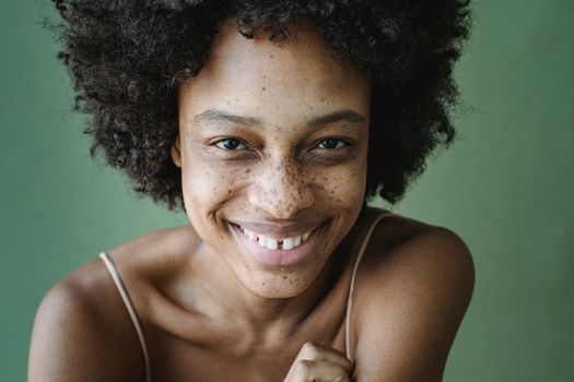 Portrait of a smiling woman with an afro hairstyle and freckles against a green background.