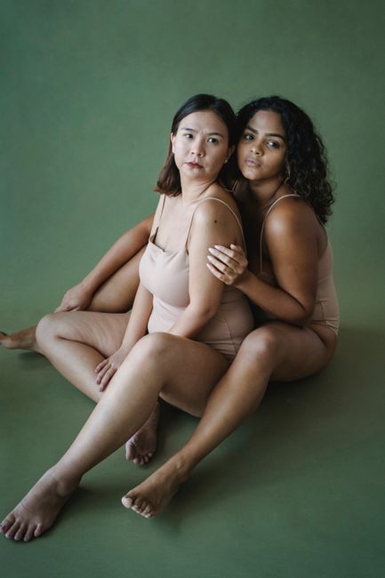 Studio portrait of two diverse women embracing with a green background.