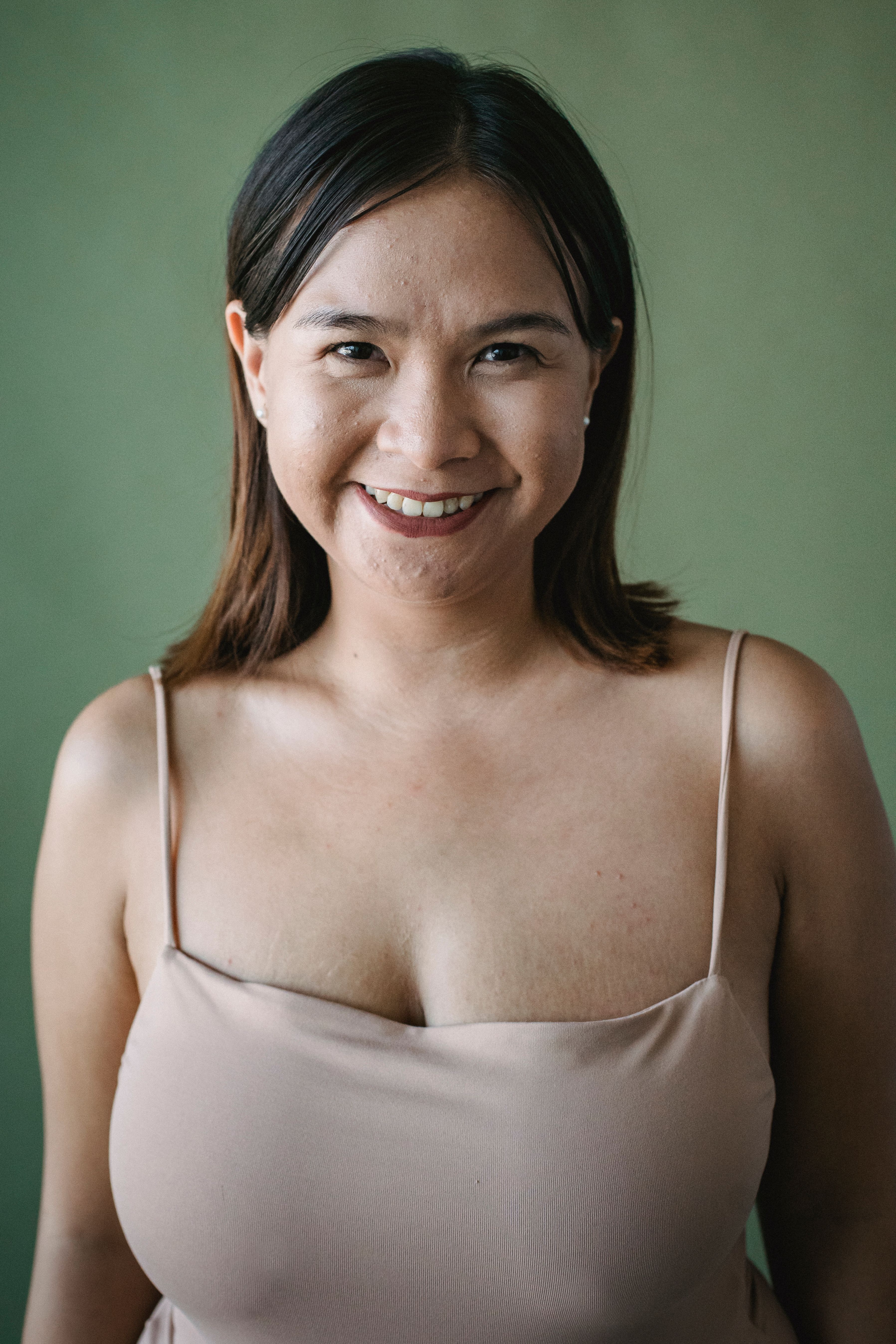 绿色背景下，一位穿着意面肩带上衣的女士微笑的肖像