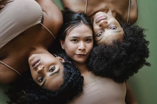 Free A close-up portrait of three diverse women lying down with different hair textures and skin tones. Stock Photo