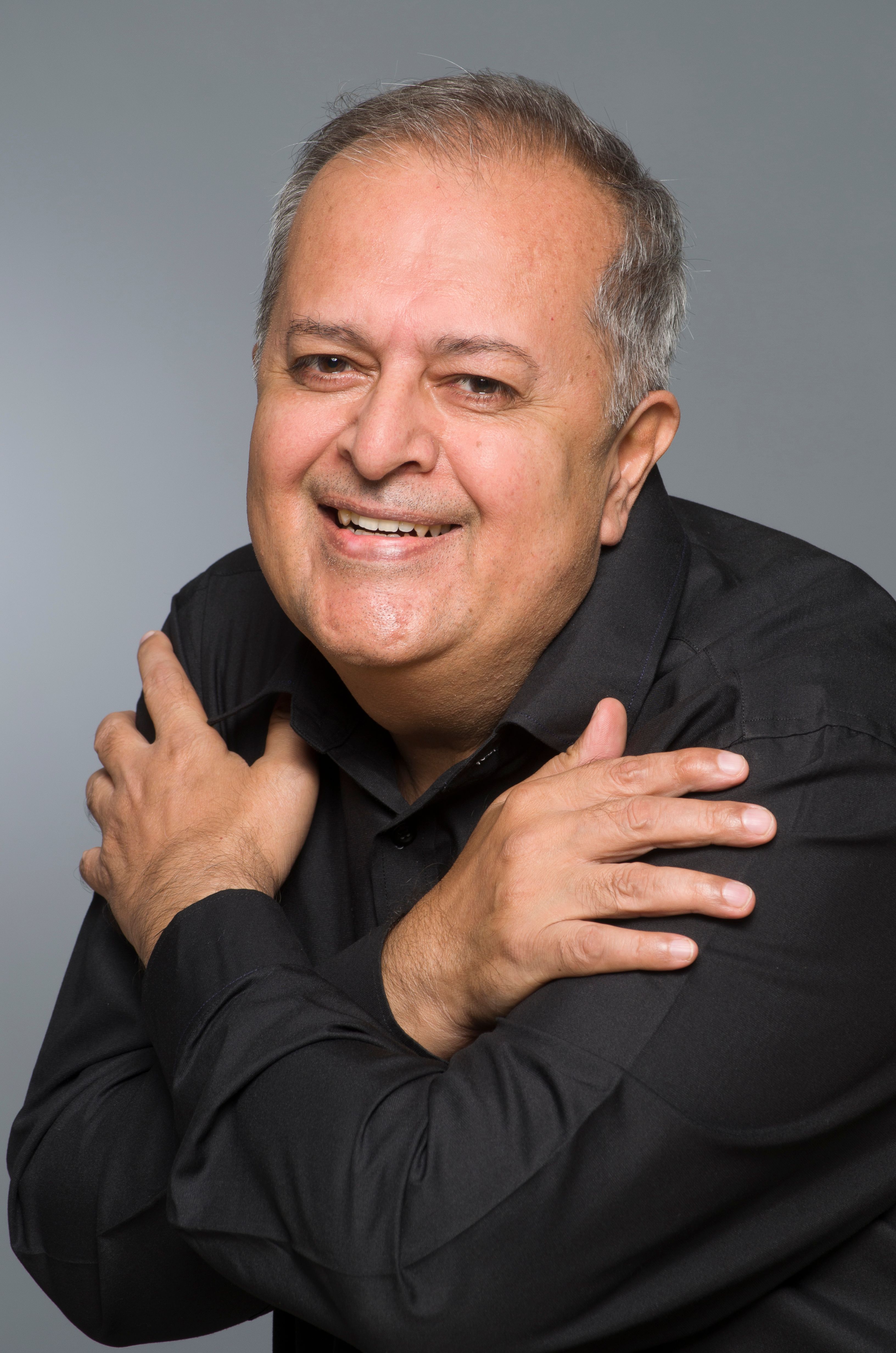 Smiling senior man in black shirt embraces himself in a studio portrait.