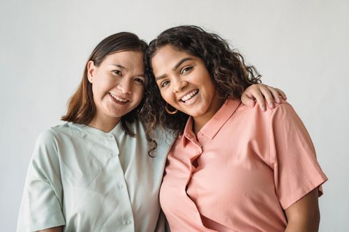 Free Two women smiling with arms around each other in a studio portrait on a white background. Stock Photo