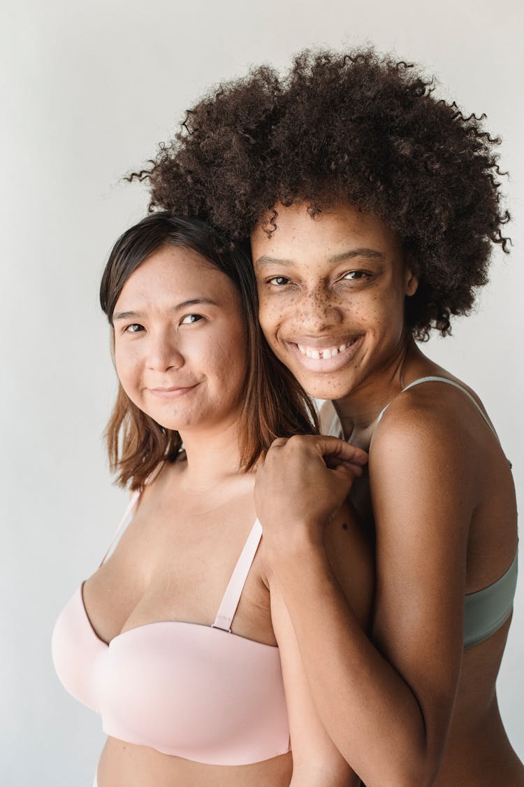 Portrait Of Two Women In Pastel Bras Against White Background