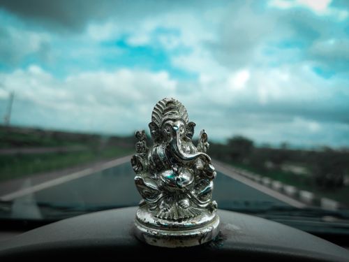 Free Silver Ganesh statue on a car dashboard symbolizing spirituality against a cloudy sky. Stock Photo