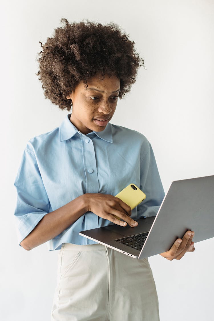 Studio Shot Of A Woman With Afro Hairstyle Holding A Phone And Laptop