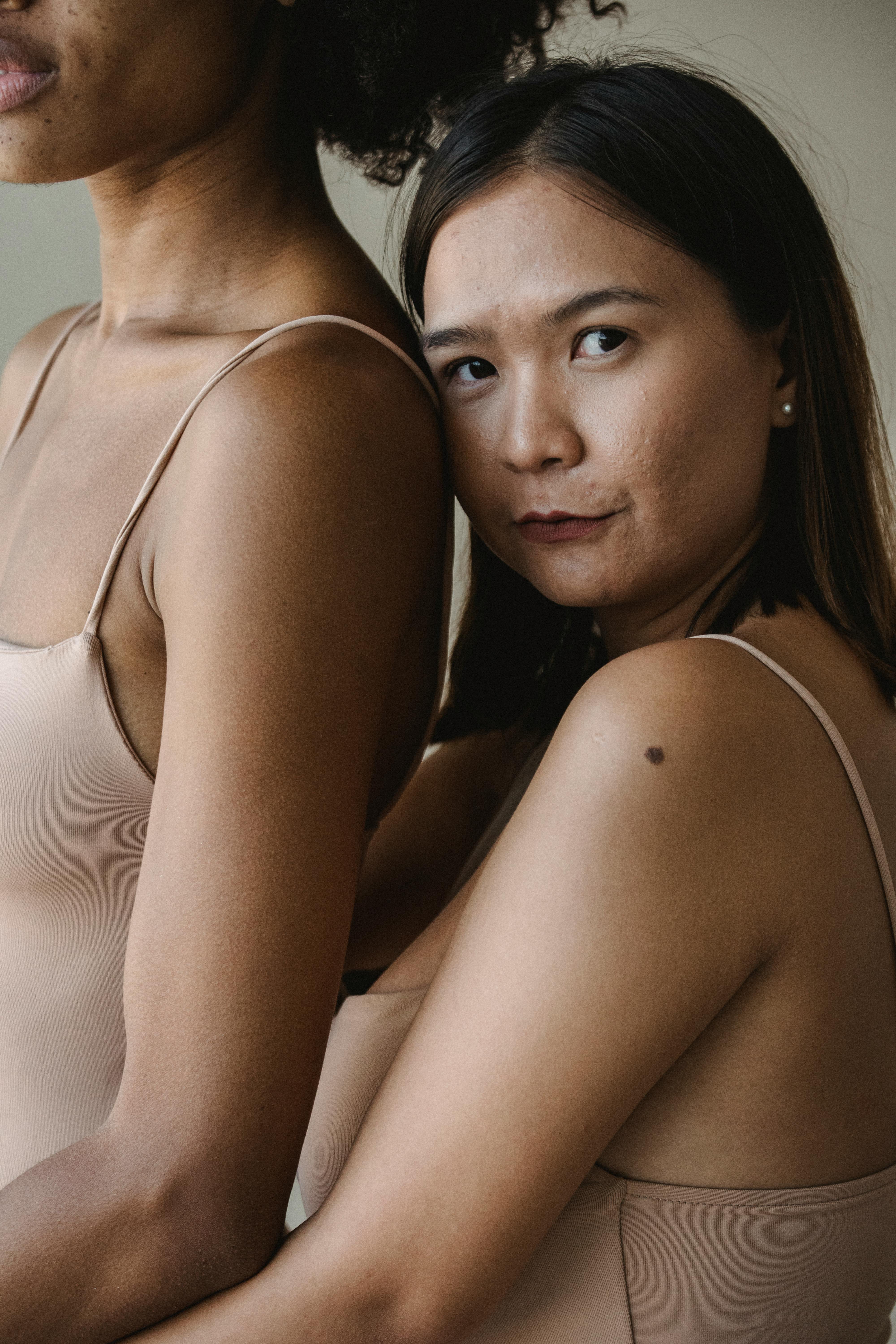 Two women with diverse ethnic backgrounds embracing in a studio setting, promoting unity and diversity.