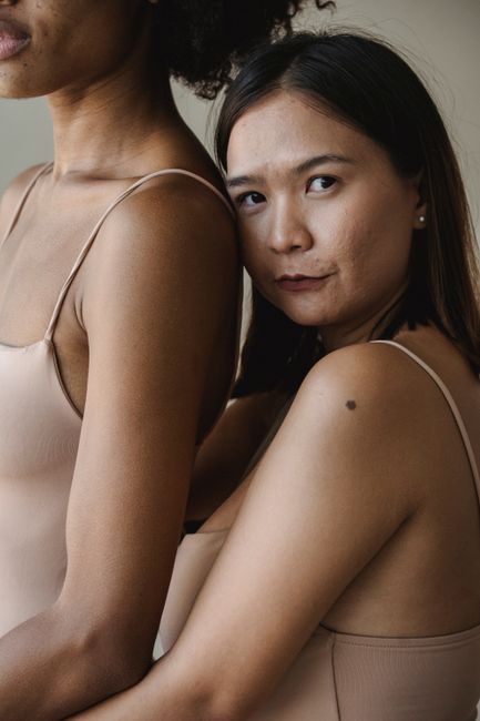 Two women with diverse ethnic backgrounds embracing in a studio setting, promoting unity and diversity.