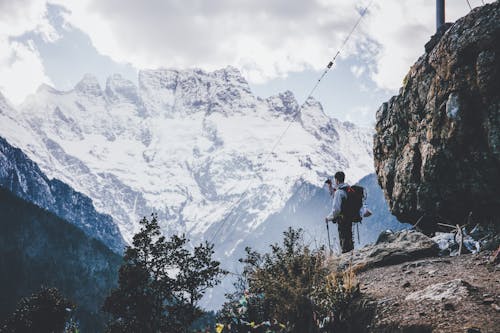 Side view of male alpinist with backpack and trekking sticks standing on edge of cliff and enjoying view of highland
