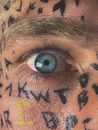Crop male with wide opened blue eye and Latin alphabet letters painted on face skin staring at camera