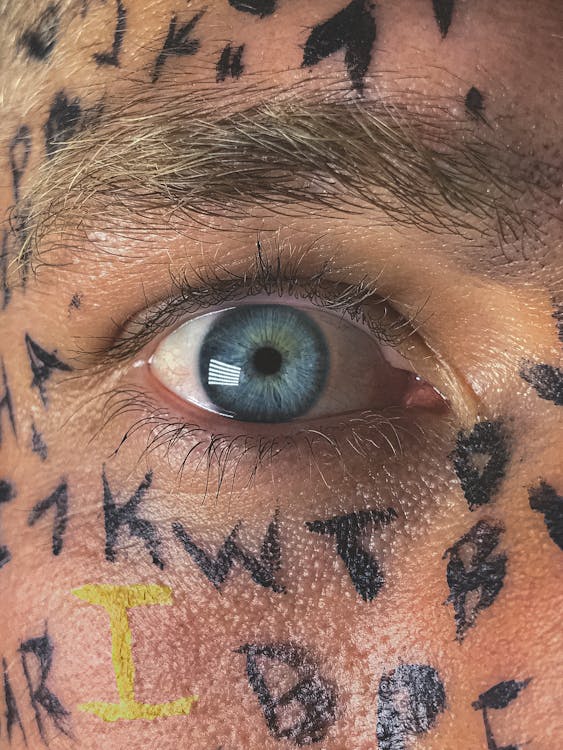 Free Crop male with wide opened blue eye and Latin alphabet letters painted on face skin staring at camera Stock Photo