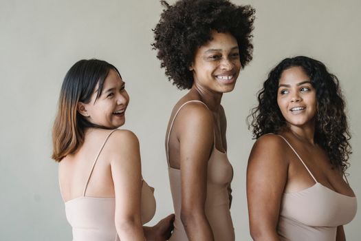 Three diverse women smiling and embracing body positivity in a studio setting.