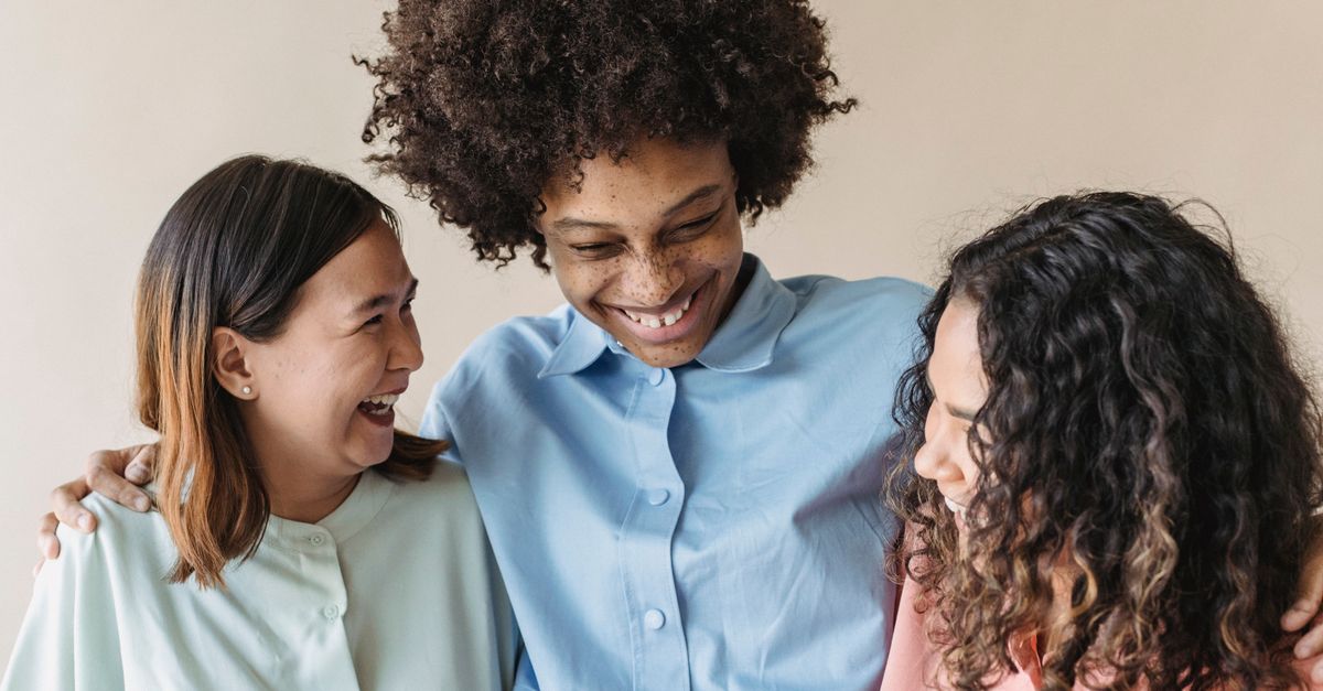 A joyful portrait of three diverse women embracing and smiling together, showcasing friendship.