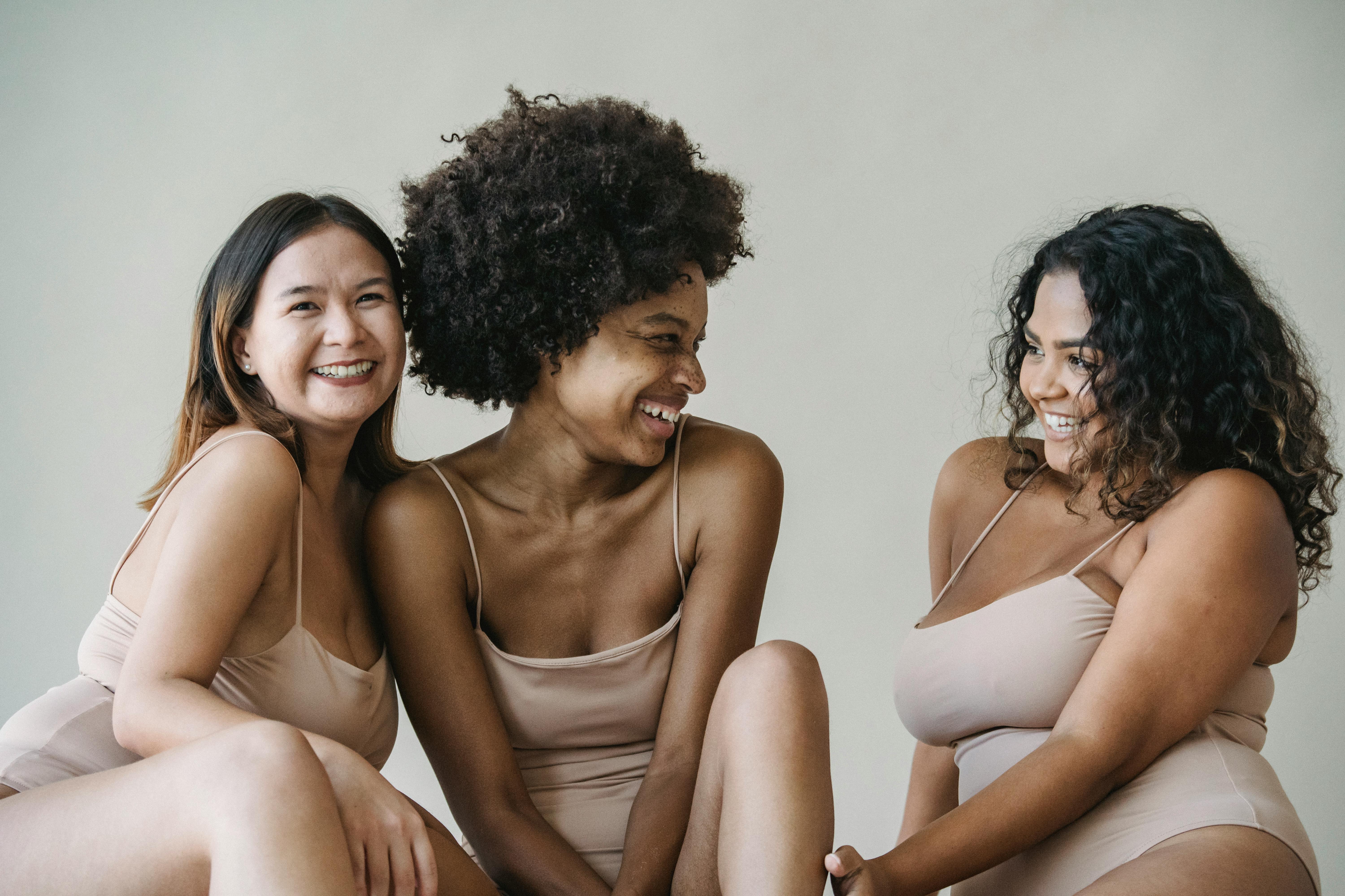 Three diverse women in nude underwear smiling and enjoying a moment of body positivity and empowerment.