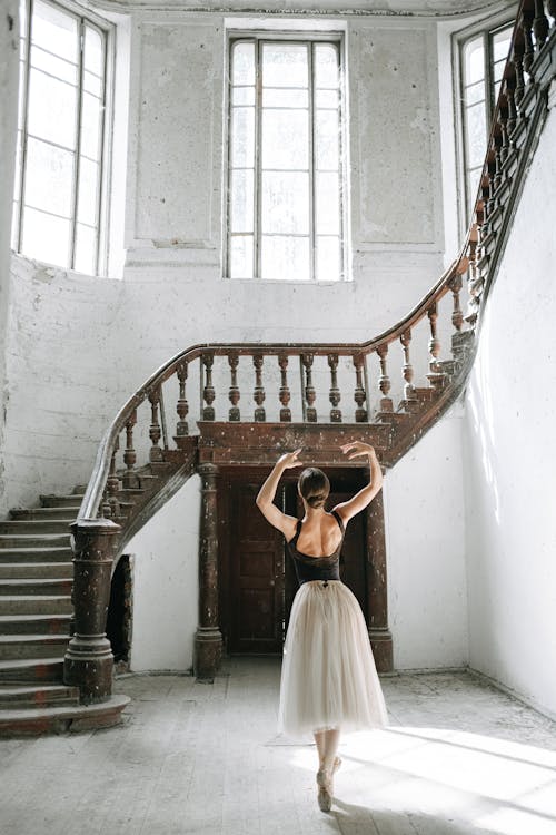 A Ballerina Dancing on Wooden Floor Near Staircase