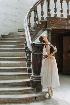 A graceful ballerina in a flowing dress poses on an antique staircase in an old, rustic building.
