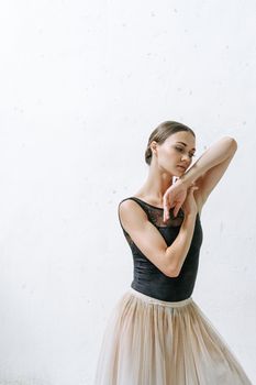 Elegant ballerina in a black tank top and skirt poses gracefully against a minimalist white background.