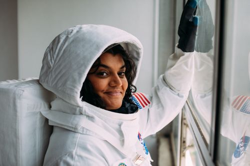Free Portrait of a woman in a white astronaut costume smiling while looking out of a window. Stock Photo