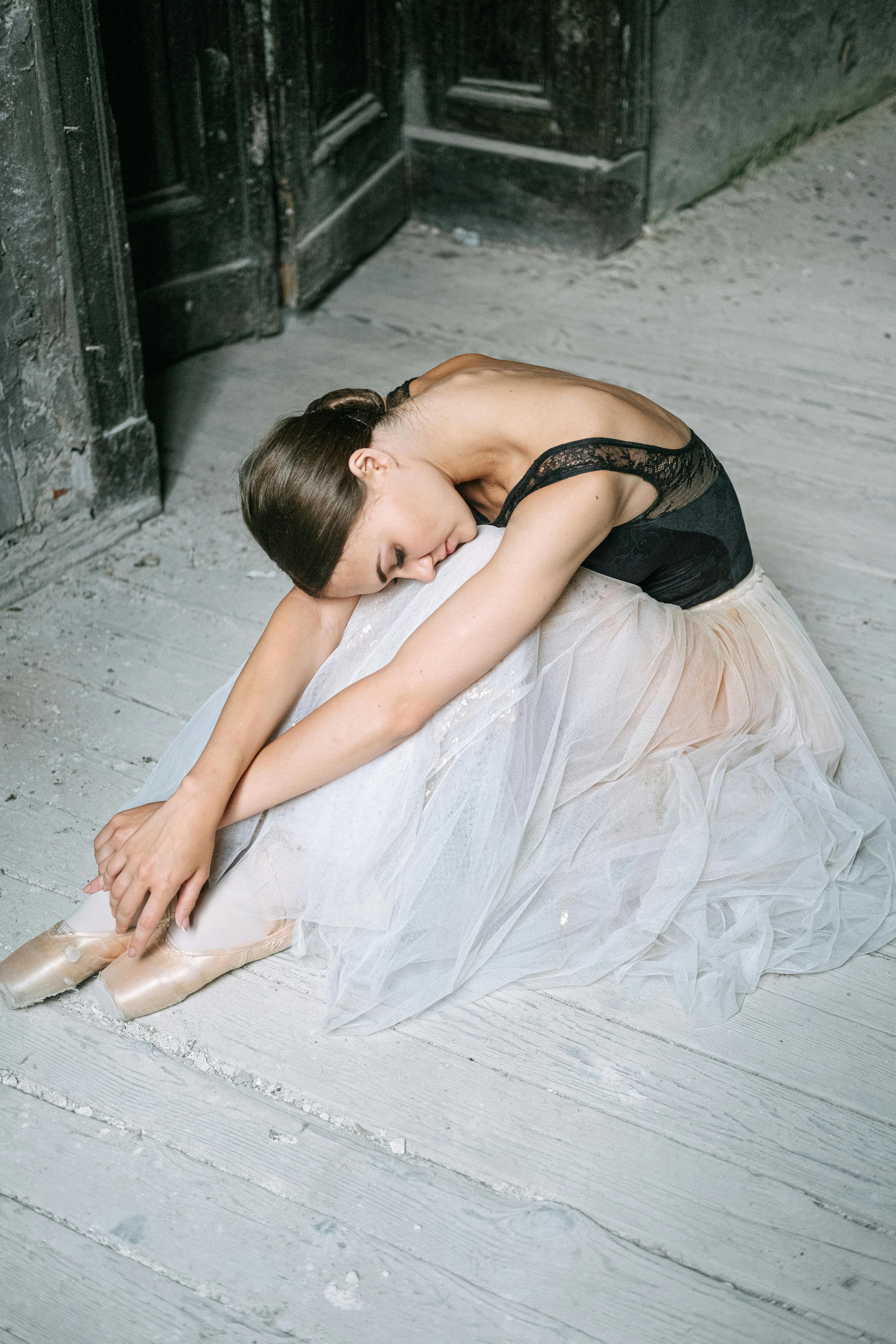 一位身着黑色上衣和白色芭蕾舞短裙的优雅芭蕾舞演员，正优雅地坐在室内的木地板上