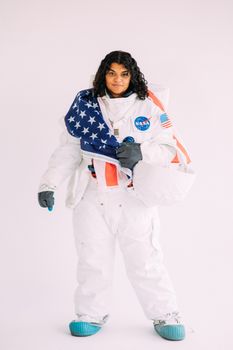 在朴素的背景下，一位穿着美国宇航局宇航员服的妇女举着美国国旗的肖像