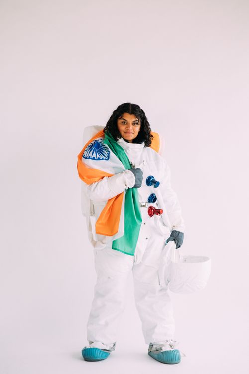 Free Indian woman in astronaut suit holding the national flag of India, symbolizing exploration. Stock Photo