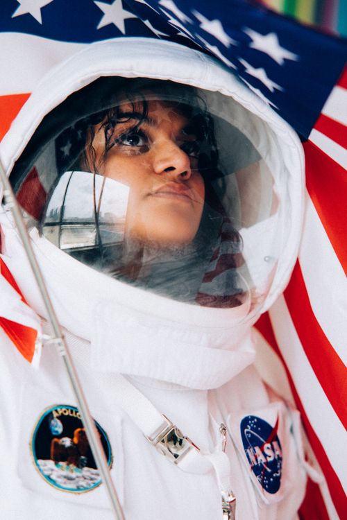 Free Close-up of a woman in an astronaut suit holding an American flag, symbolizing exploration. Stock Photo