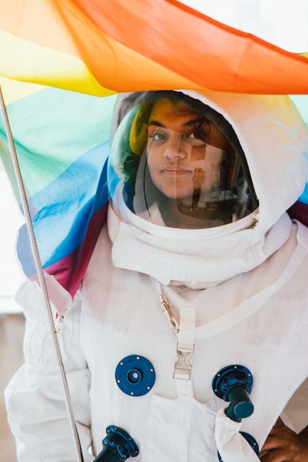 A woman in an astronaut suit holding a rainbow flag, symbolizing diversity.