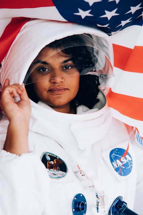 Free A woman wearing an astronaut suit holding an American flag, showcasing a space exploration theme. Stock Photo