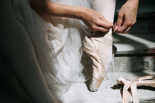 Free Ballerina preparing for performance, tying pointe shoes in soft natural light. Stock Photo