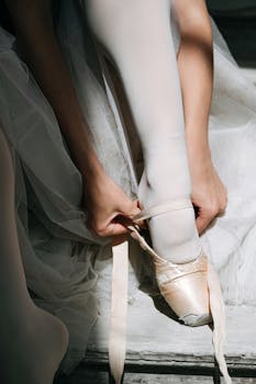 A close-up of a ballerina tying her pointe shoes in soft natural light.