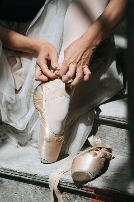 Ballerina gracefully tying pointe shoes, capturing elegance and dedication in dance.