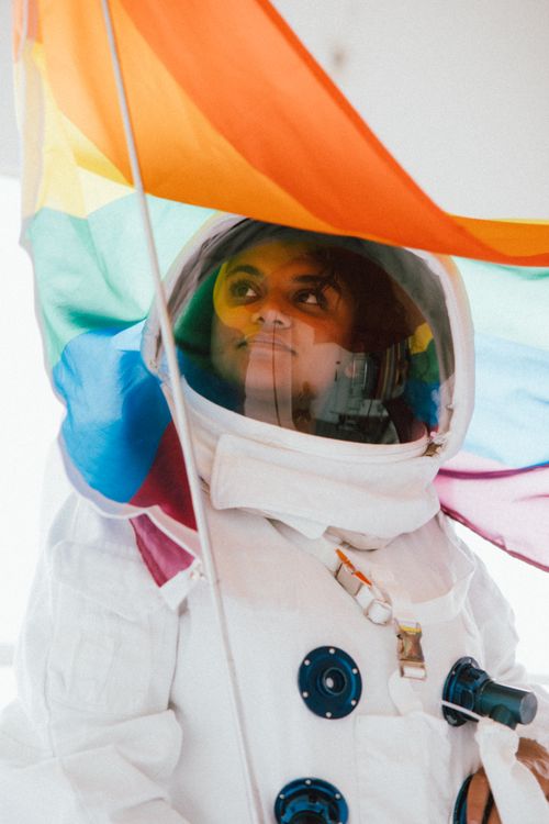 Free Woman in astronaut costume under a vibrant rainbow flag, embracing diversity. Stock Photo