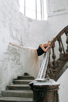 A graceful ballerina poses elegantly on a vintage staircase in an antique setting.