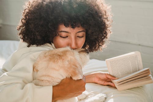 Black woman caressing with dog while reading book