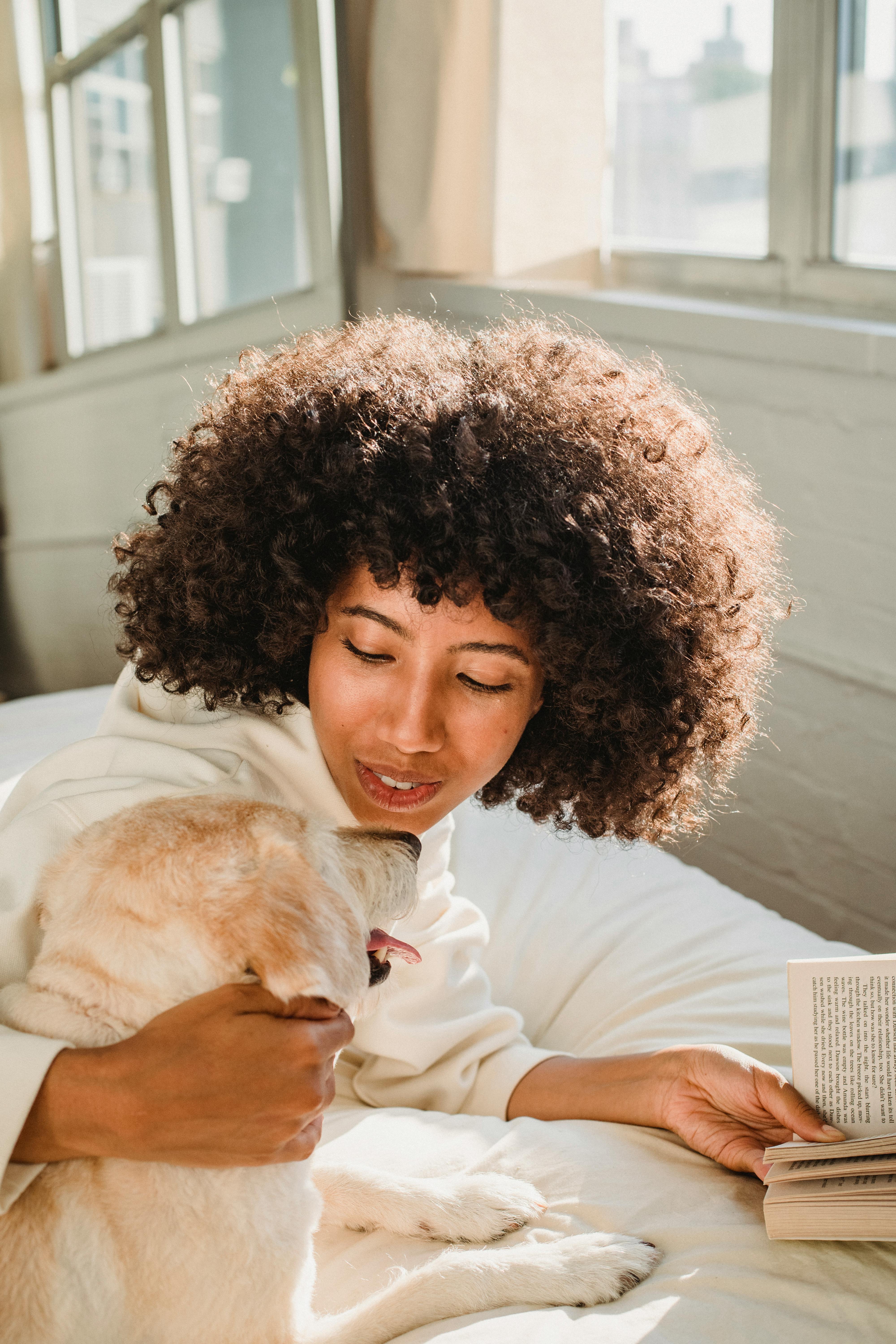 black woman hugging dog while reading book in bedroom