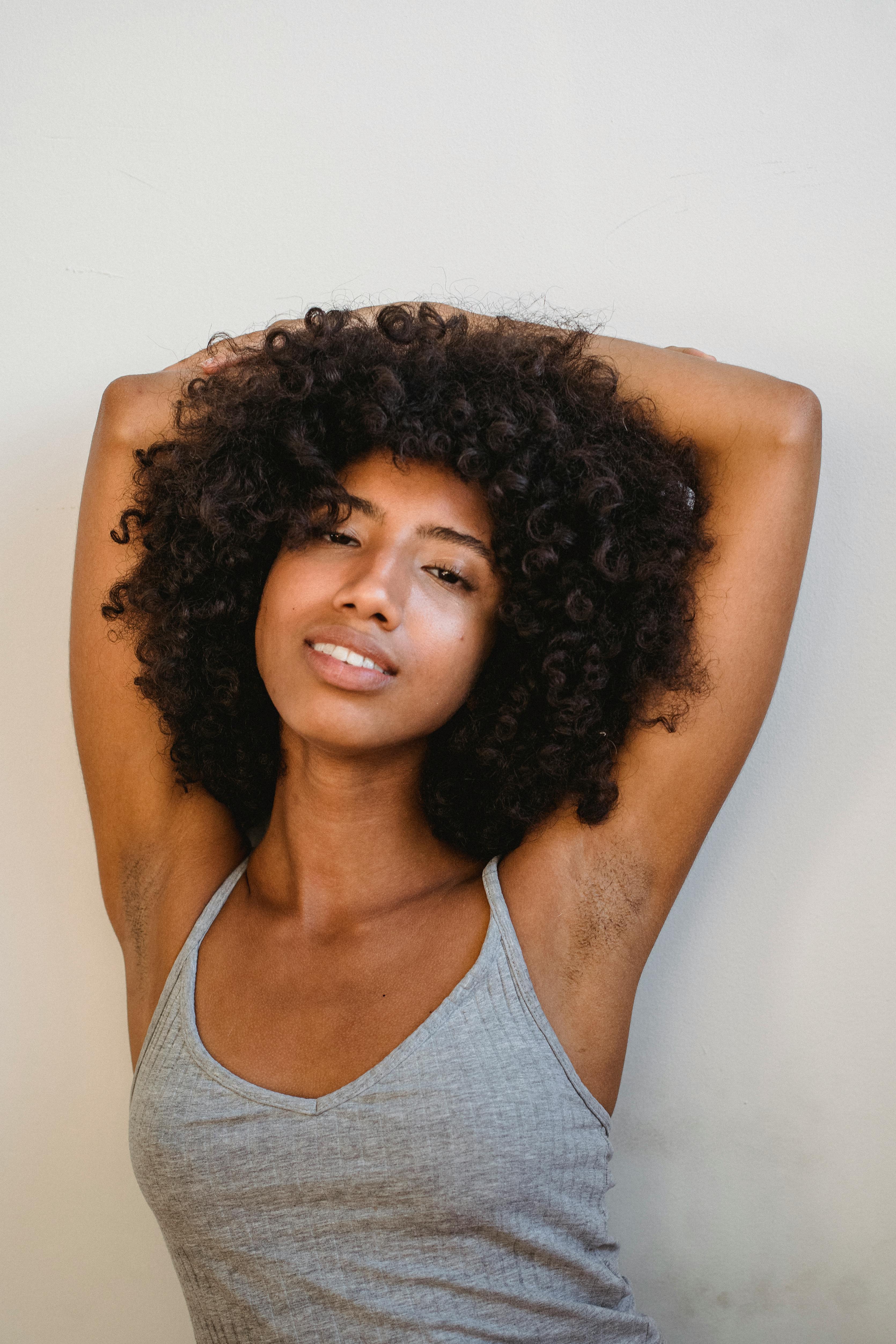 Free Photo  Relaxed smiling afro woman with fancy makeup and accessories  posing with closed eyes and crossed hands on chest, over blue wall