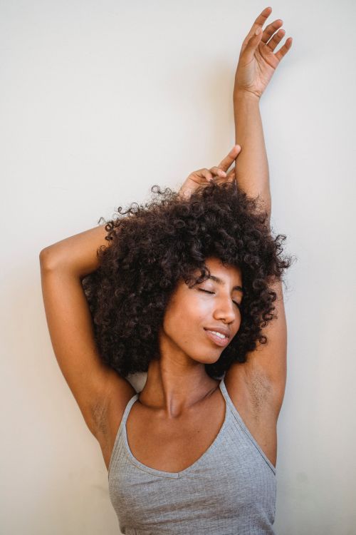 Free Young African American female smiling and raising hands while posing with eyes closed Stock Photo