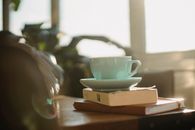 桌子上放着白色陶瓷茶杯、盘子和一本破旧的书，旁边还有笔记本
