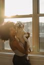 Happy black woman holding cute Labrador on hands near window