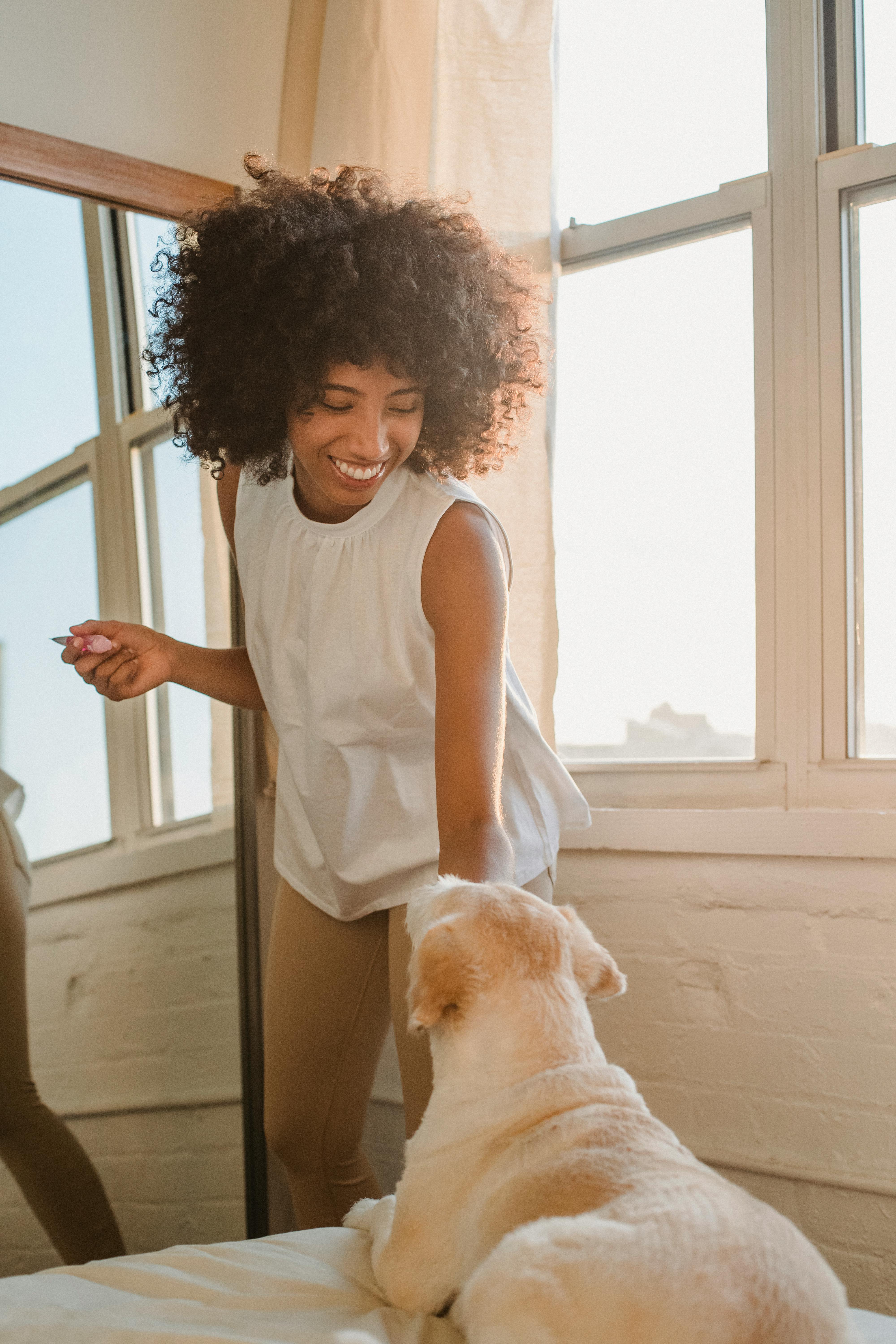 smiling black woman caressing cute labrador dog resting on bed