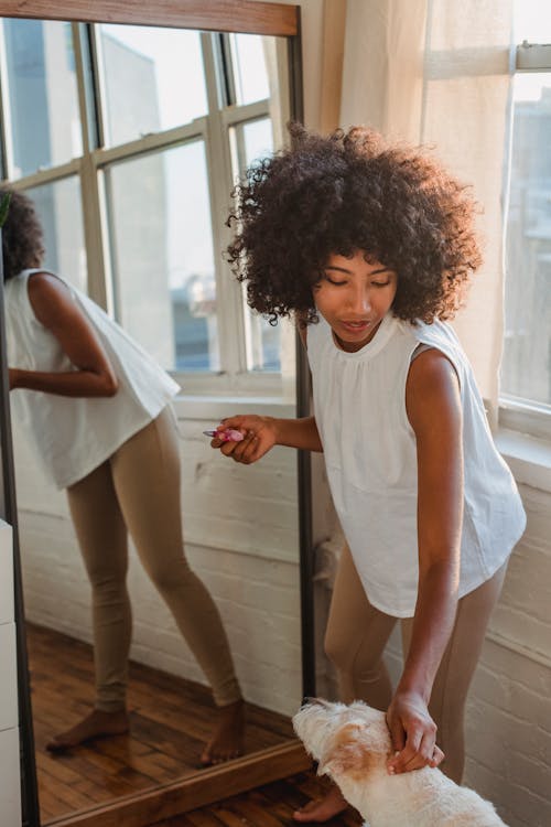 Content black woman caressing purebred dog near mirror in bedroom